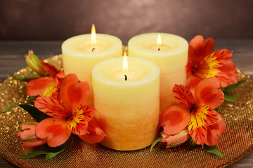 Fototapeta na wymiar Beautiful candles with flowers on table on brown background