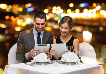 couple with menus on tablet pc at restaurant