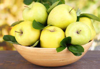 Ripe sweet apples with leaves in wooden bowl