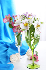 Freesias in glasses on table on fabric background
