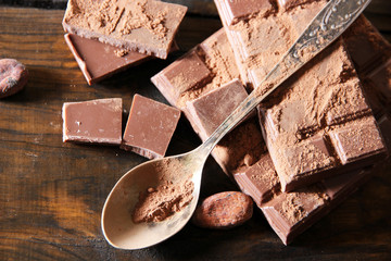 Cocoa powder and dark chocolate on color wooden background