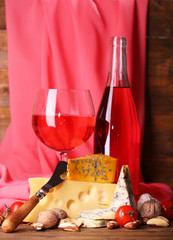 Pink wine and different kinds of cheese on fabric background
