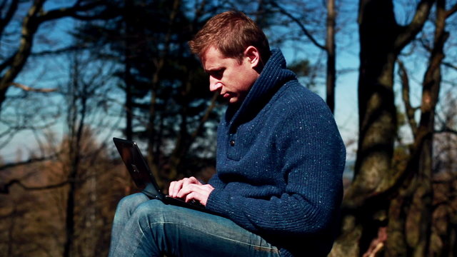 man working on a laptop and sitting in the forest