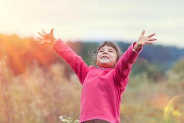 Happy little girl with hands up on the meadow in sunny day