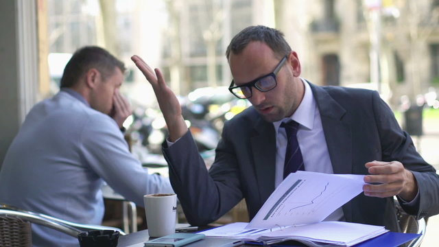 worried businessman looking at bad results in documents and sitt
