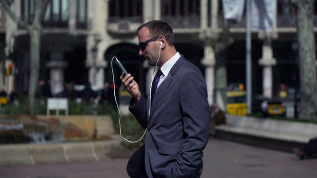 businessman with the headphones walking along the street and tal