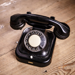 Old black phone with dust and scratches on wooden floor