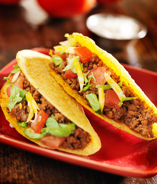 two beef tacos with cheese, lettuce and tomatos