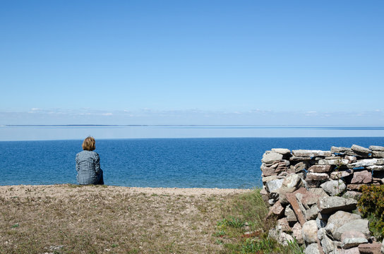 Woman sitting by the coast looking at clear blue sky and water