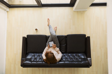 Young woman sitting on a sofa with digital tablet surfing online