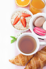 Tea cup with croissant, colourful french macaroons, oatmeal with