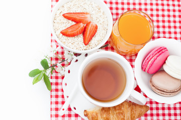 Obraz na płótnie Canvas Tea cup with croissant, colourful french macaroons, oatmeal with