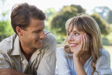 Fototapeta premium Carefree couple lying in the park smiling at each other