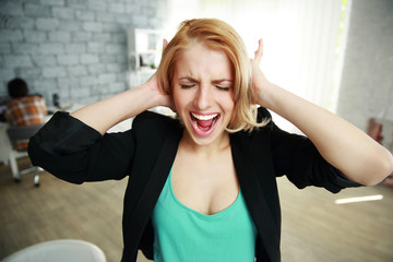 Screaming young woman with closed ears in office