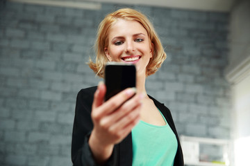 Young smiling woman holding smartphone in office