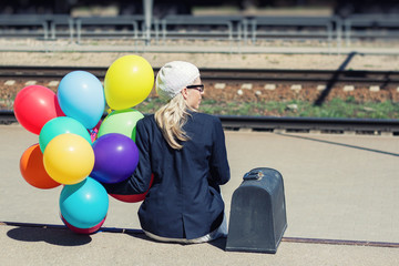 Young woman with colorful balloons sitting at railroad tracks