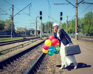 Young woman with colorful balloons on railroad platform