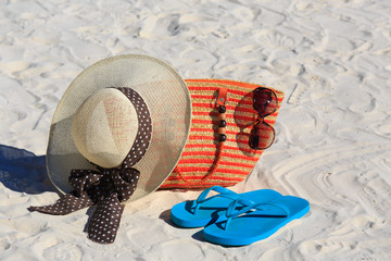 Straw hat, bag, sun glasses and flip flops on a sand beach