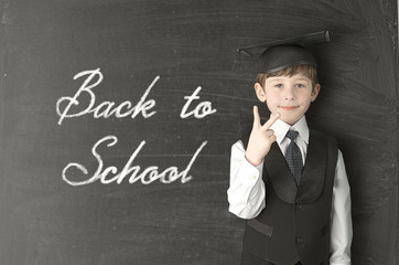 Cheerful little boy on blackboard. Looking at camera