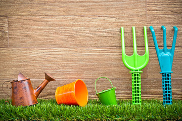 watering cans, pails, fork, rake on grass with wood background