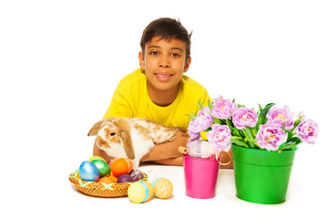 Boy lying and hugging rabbit near Eastern eggs