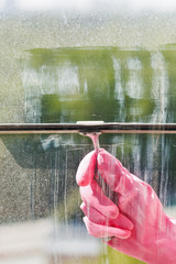 hand in pink glove washes window pane by squeegee