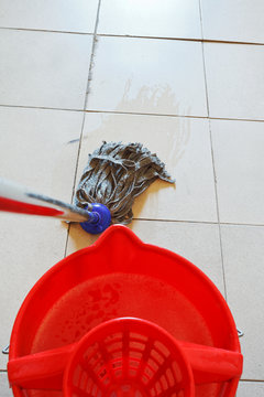 cleaning the tile floor by swab and red bucket
