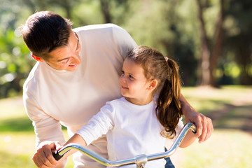 young father riding bicycle with his daughter