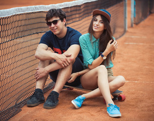 Couple sitting on a skateboard on the tennis court