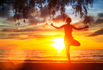Silhouette of girl practicing yoga on the beach at sunset.