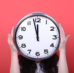 Portrait of girl holding huge office clock against red backgroun