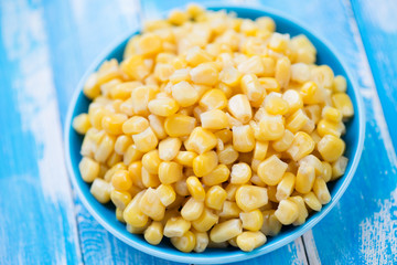 Glass plate with sweet corn kernels over blue wooden background
