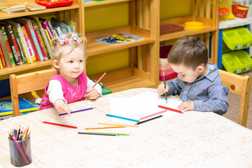 Two little kids drawing with colorful pencils in preschool