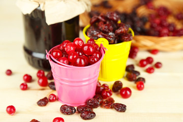 Fresh and dry cranberry in pails on wooden table close-up