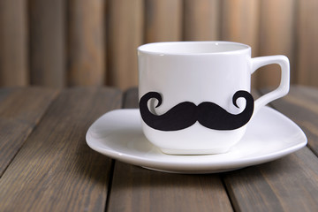Cup with mustache on table on wooden background