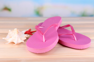 Bright flip-flops on wooden table, on nature background