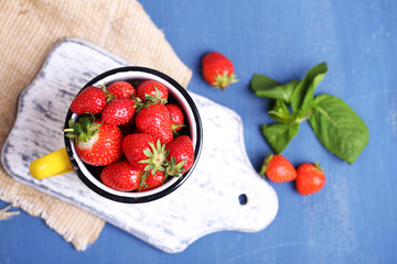 Ripe sweet strawberries in mug  on color wooden background