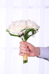 Male hand holding wedding bouquet on light background