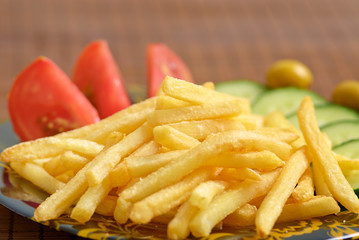 Close up of french fries with cucumber, tomato and olives