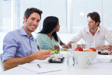 Workers chat and smile to camera while enjoying lunch