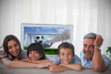 Family smiling at the camera with world cup showing on televisio