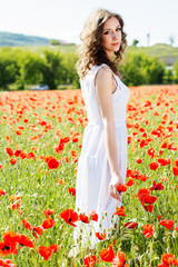 Obraz na płótnie Canvas Young beautiful girl in the field of poppies