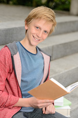 Happy teenage boy studying sitting on stairs