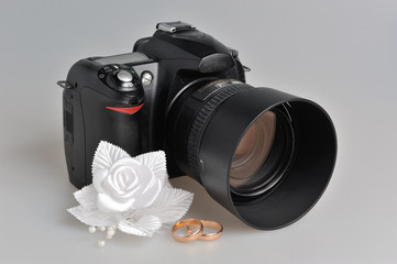 Photo camera, wedding boutonniere, rings on gray