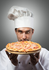 Humorous portrait of a man in chef's hat smelling pizza