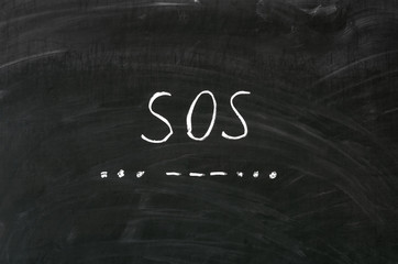SOS word handwritten with white chalk on a blackboard