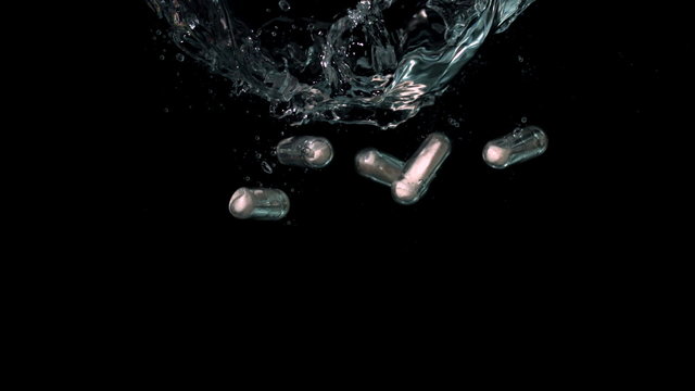 White pills falling in water on black background