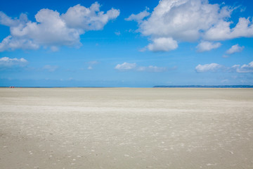 ocean at low tide under blue cloudy sky, at Mont Saint Michelle