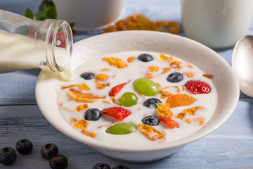 Pouring milk on cornflakes with fruits