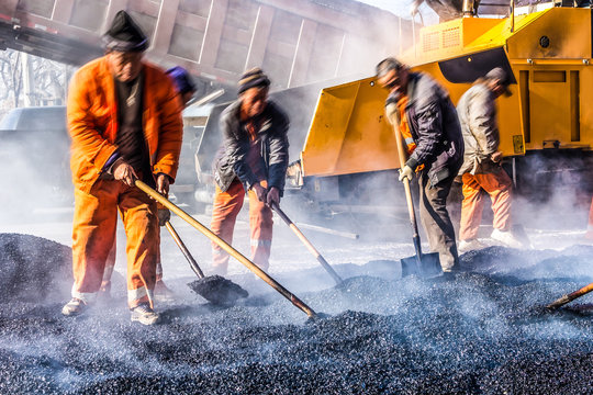Workers making asphalt with shovels at road constructio